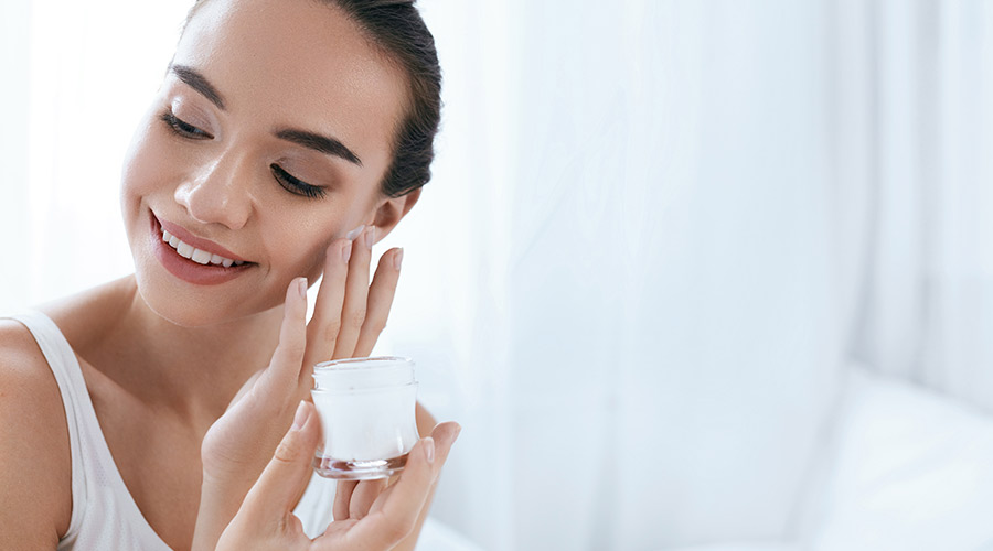 Ácidos para pele: jovem mulher aplica produto no rosto.