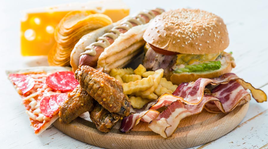 As dietas não saudáveis podem ser uma causa da calvície precoce. Na imagem estão retratadas vários tipos de fast food, como hamburger, pizza e cachorro quente.