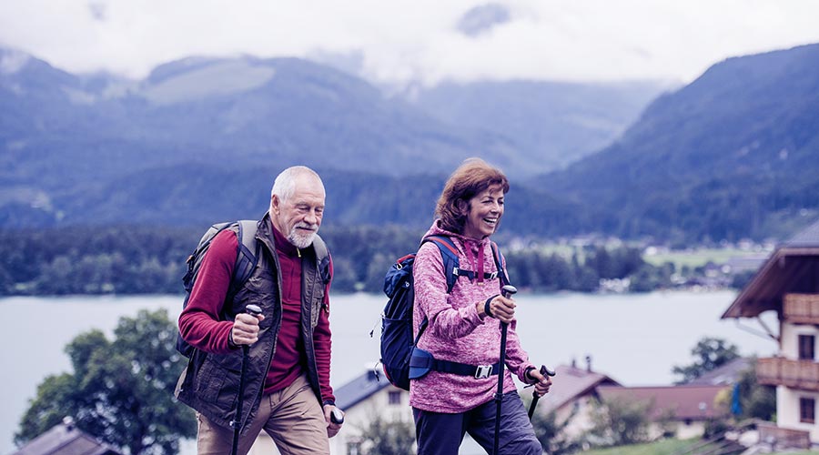 A imagem mostra um homem e uma mulher na terceira idade fazendo trekking.